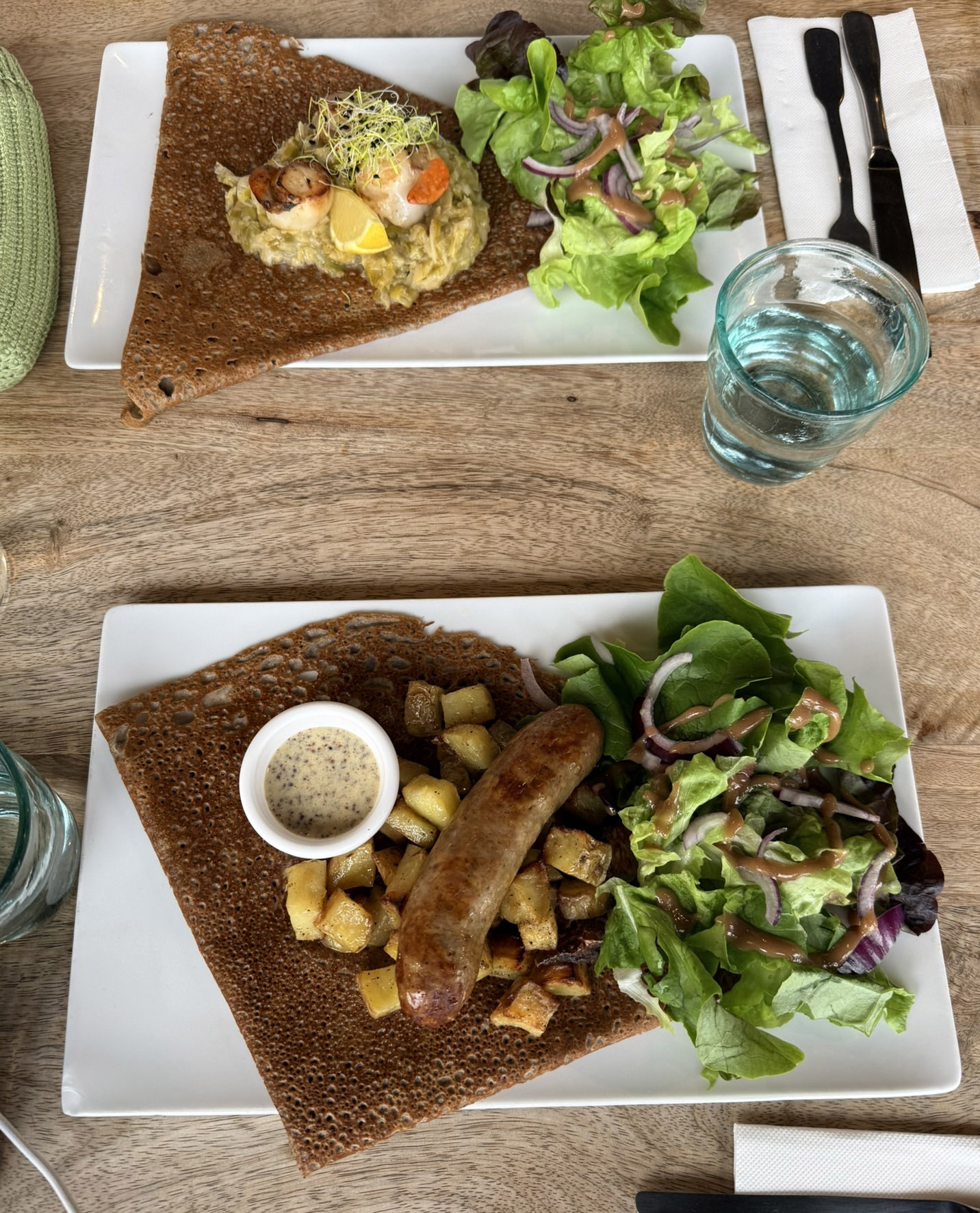 两个荞麦薄饼，上为扇贝和韭葱酱，下为香肠配炸土豆和黄芥末